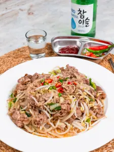 Stir fried beef brisket with bean sprouts served on a white plate with sesame seeds