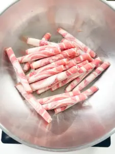 Paper thin beef brisket slices raw on a white plate before cooking