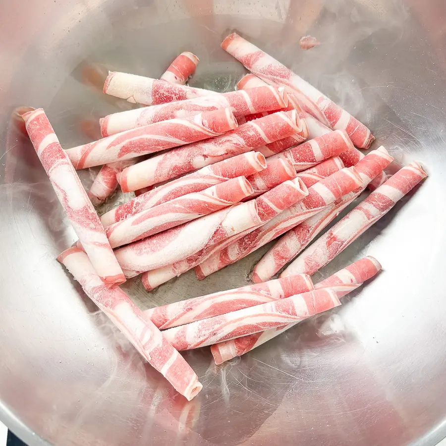 Paper thin beef brisket slices raw on a white plate before cooking