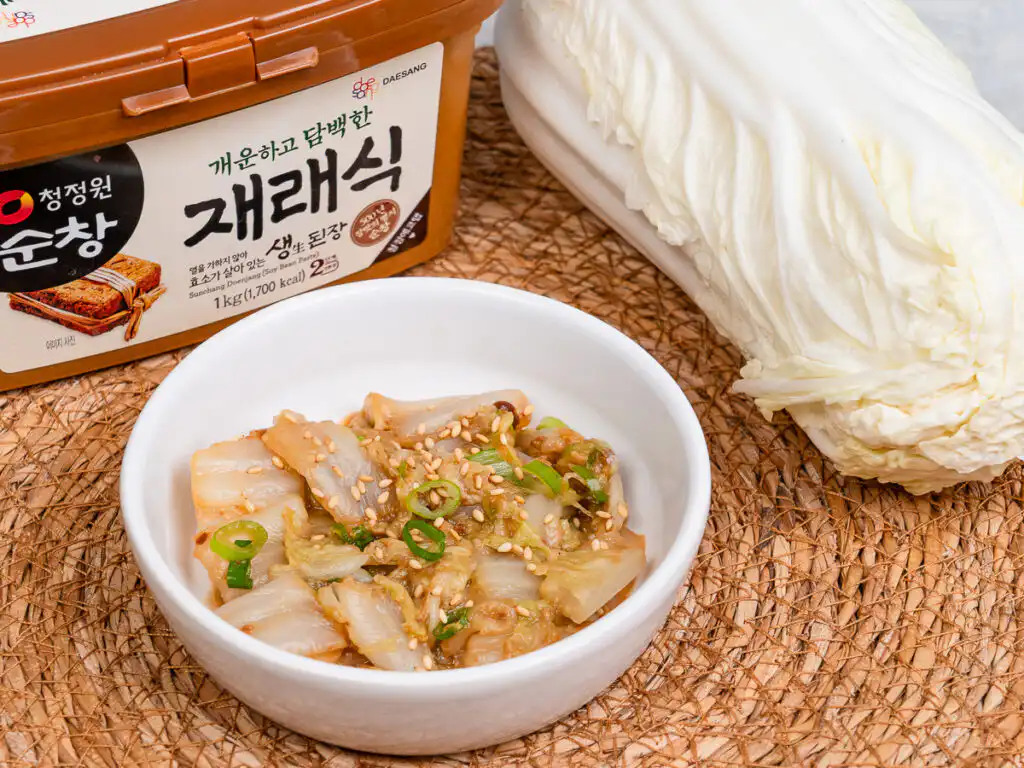Best Korean Cabbage Side Dish Recipe – Doenjang Baechu Namul korean cabbage side dish baechu namul plated on round white plate with toasted sesame seeds scattered on top