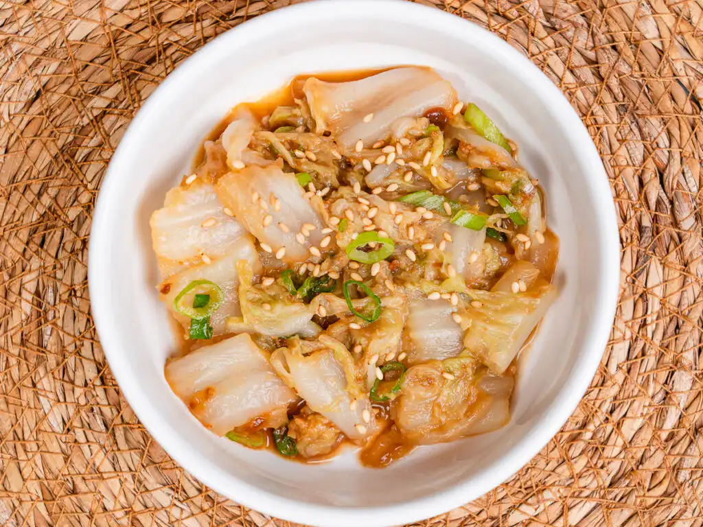 authentic korean cabbage side dish baechu namul in white ceramic bowl with sesame seeds and green onion garnish