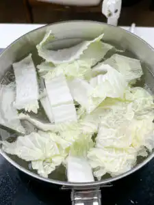 napa cabbage blanching in salted boiling water in a silver pot for baechu namul korean side dish