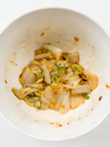adding doenjang sauce to blanched cabbage by hand in a mixing bowl for authentic korean cabbage side dish