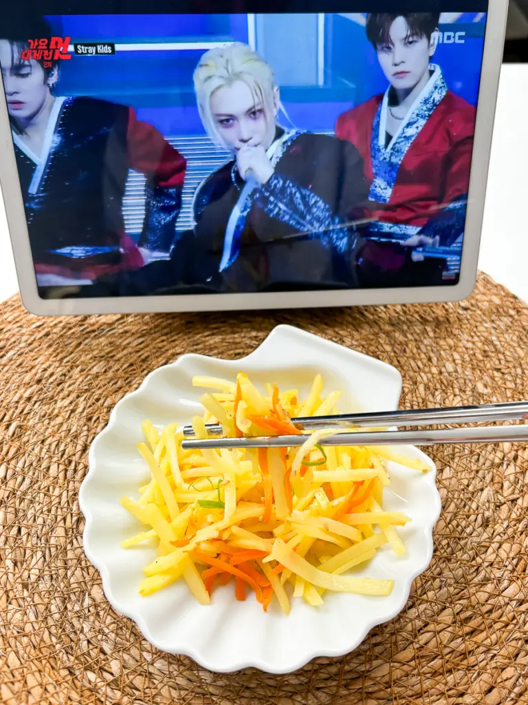 Korean potato side dish gamja bokkeum with chopsticks lifting a portion of golden potatoes