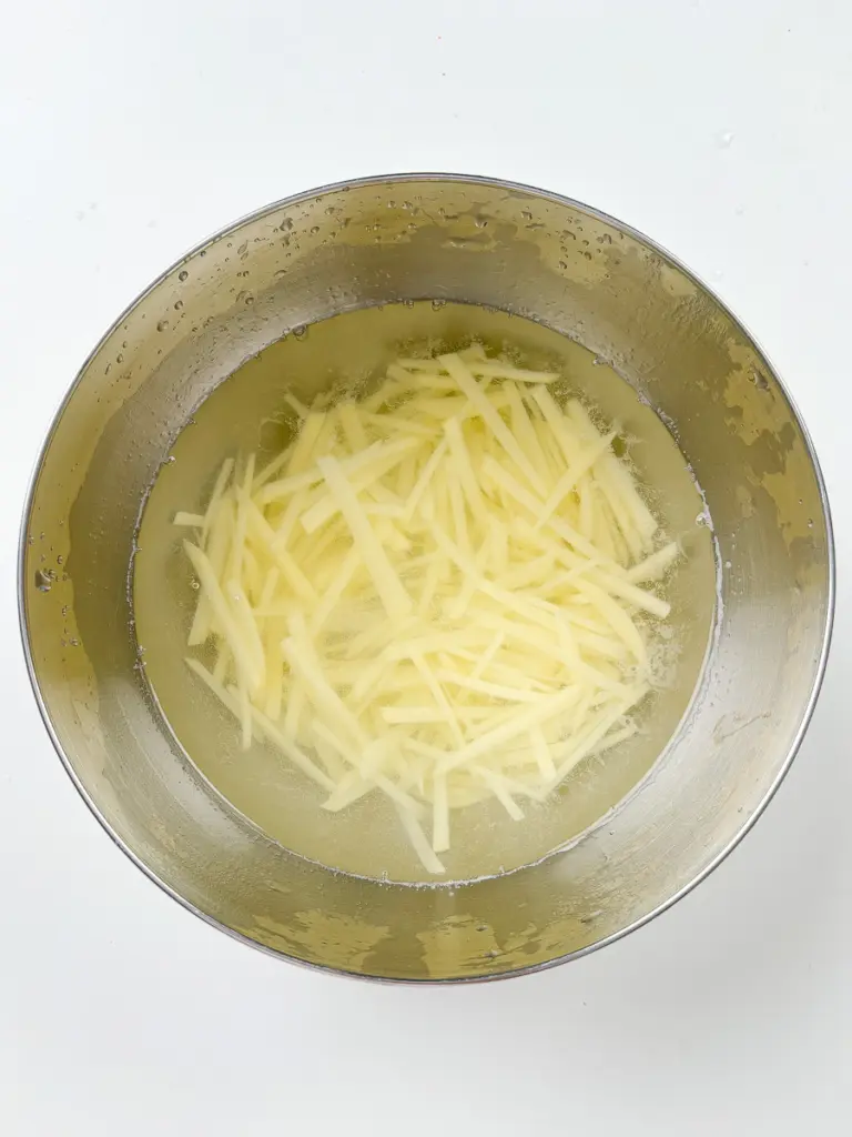 Julienned potatoes soaking in cold water to remove starch for gamja bokkeum Korean potato side dish