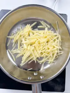 Stir frying golden potato strips in a large pan for Korean potato side dish gamja bokkeum