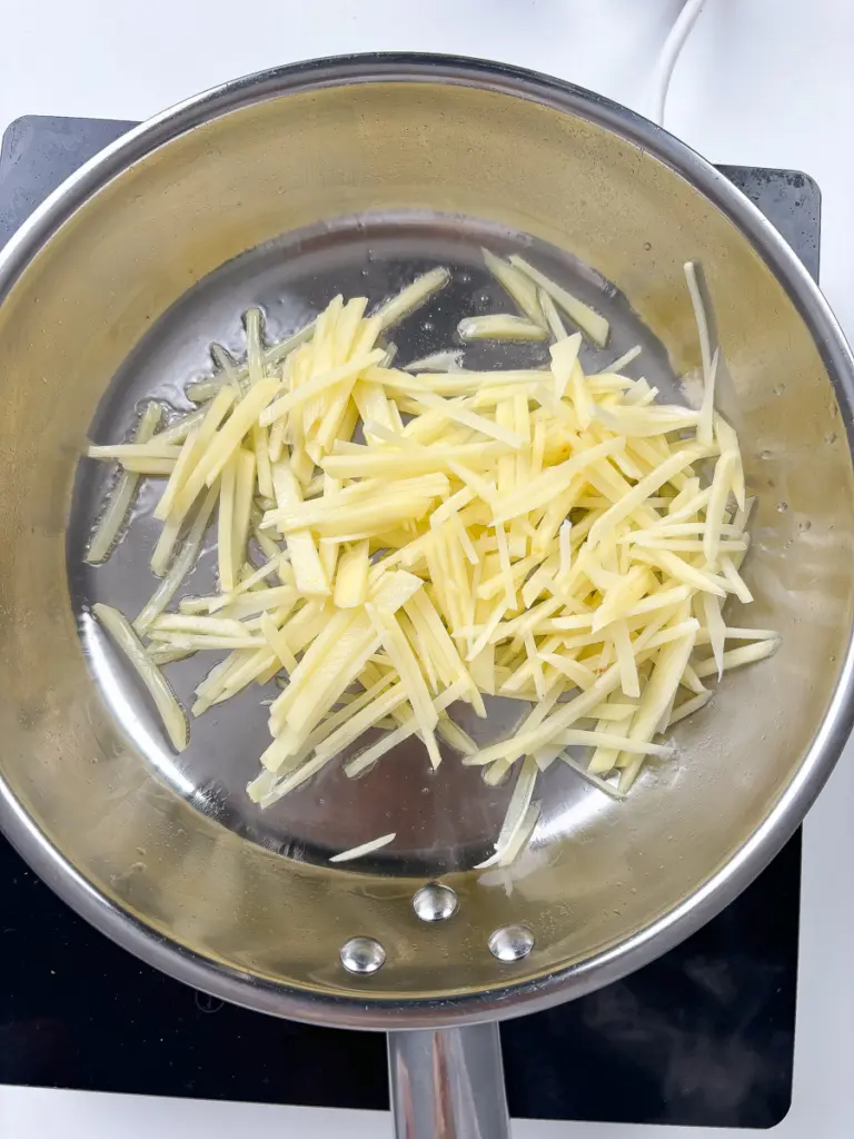 Stir frying golden potato strips in a large pan for Korean potato side dish gamja bokkeum
