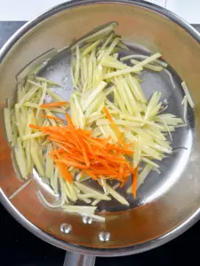 Julienned carrots added to halfway cooked potatoes in pan for gamja bokkeum with carrots recipe