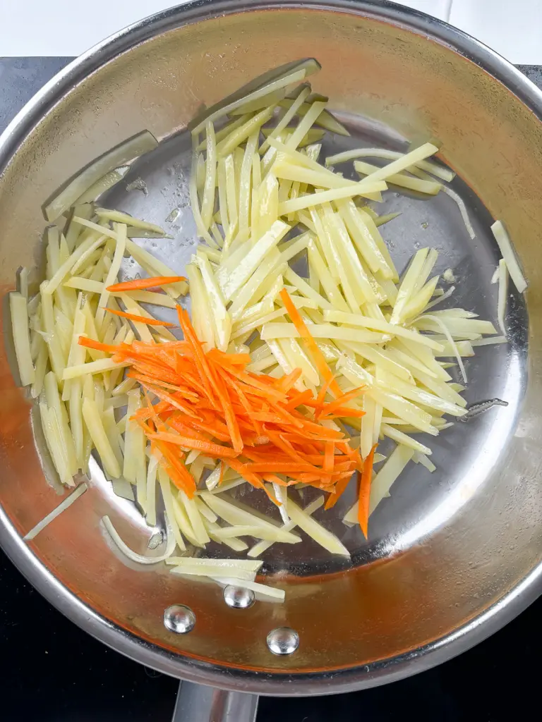 Julienned carrots added to halfway cooked potatoes in pan for gamja bokkeum with carrots recipe