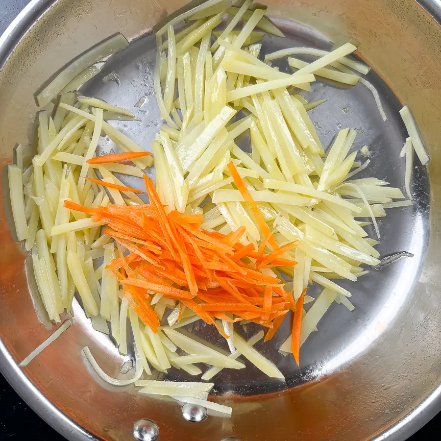 Julienned carrots added to halfway cooked potatoes in pan for gamja bokkeum with carrots recipe