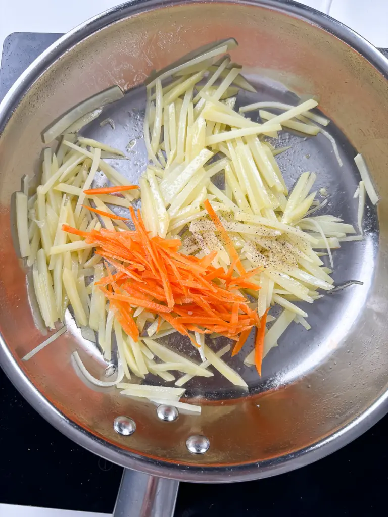 Julienned carrots added to halfway cooked potatoes in pan for gamja bokkeum with carrots recipe