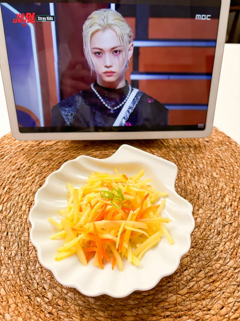 Finished gamja bokkeum being transferred from pan to serving plate Korean banchan potato dish