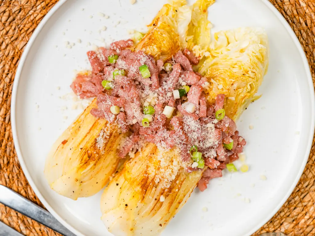 pan fried cabbage steaks with bacon and parmesan on a white ceramic plate