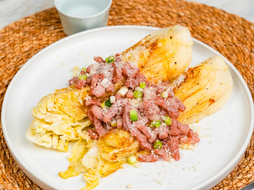 two servings of pan fried cabbage steaks with cheese on dinner table