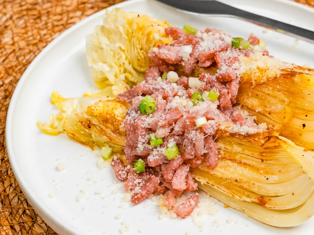 plated pan fried cabbage steaks with cheese bacon and scallions on white ceramic plate