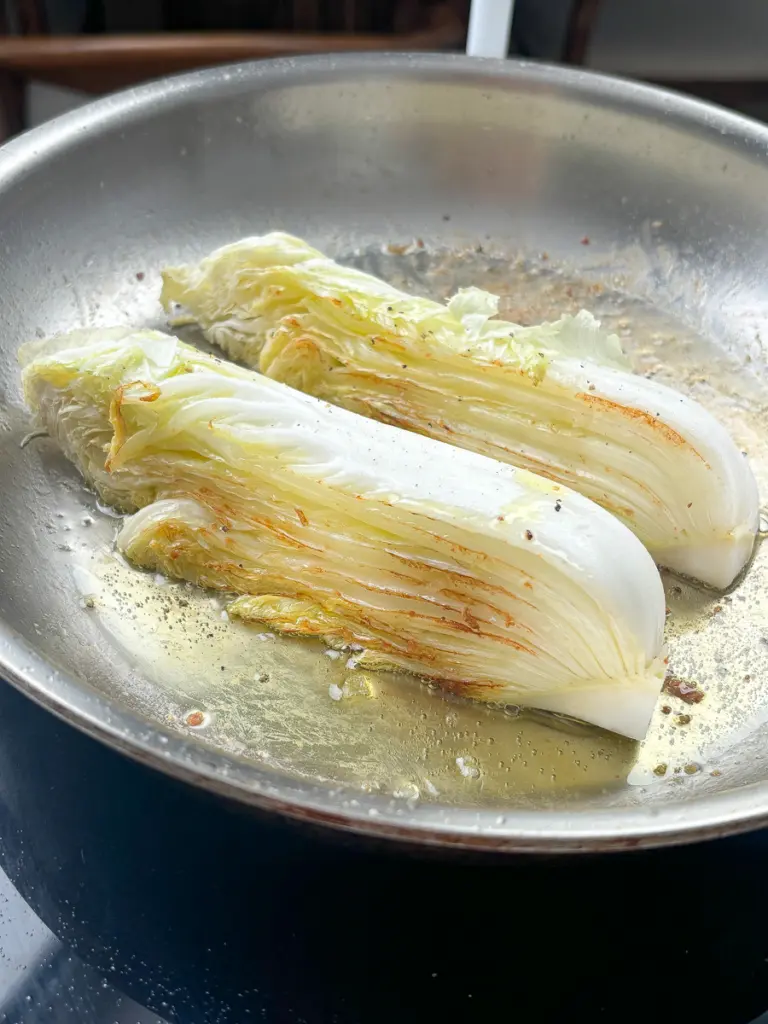 napa cabbage steaks searing in bacon fat developing deep golden brown char in cast iron pan