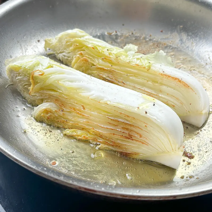 napa cabbage steaks searing in bacon fat developing deep golden brown char in cast iron pan