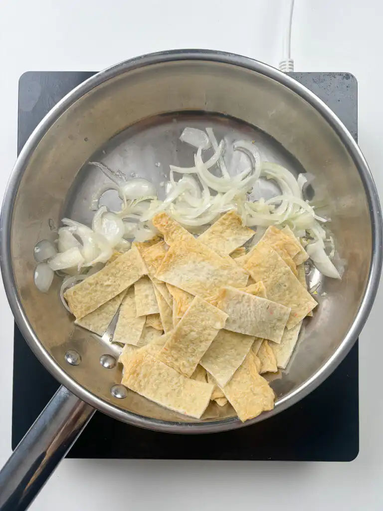 Stir fried fish cake being tossed with onion and garlic in a pan