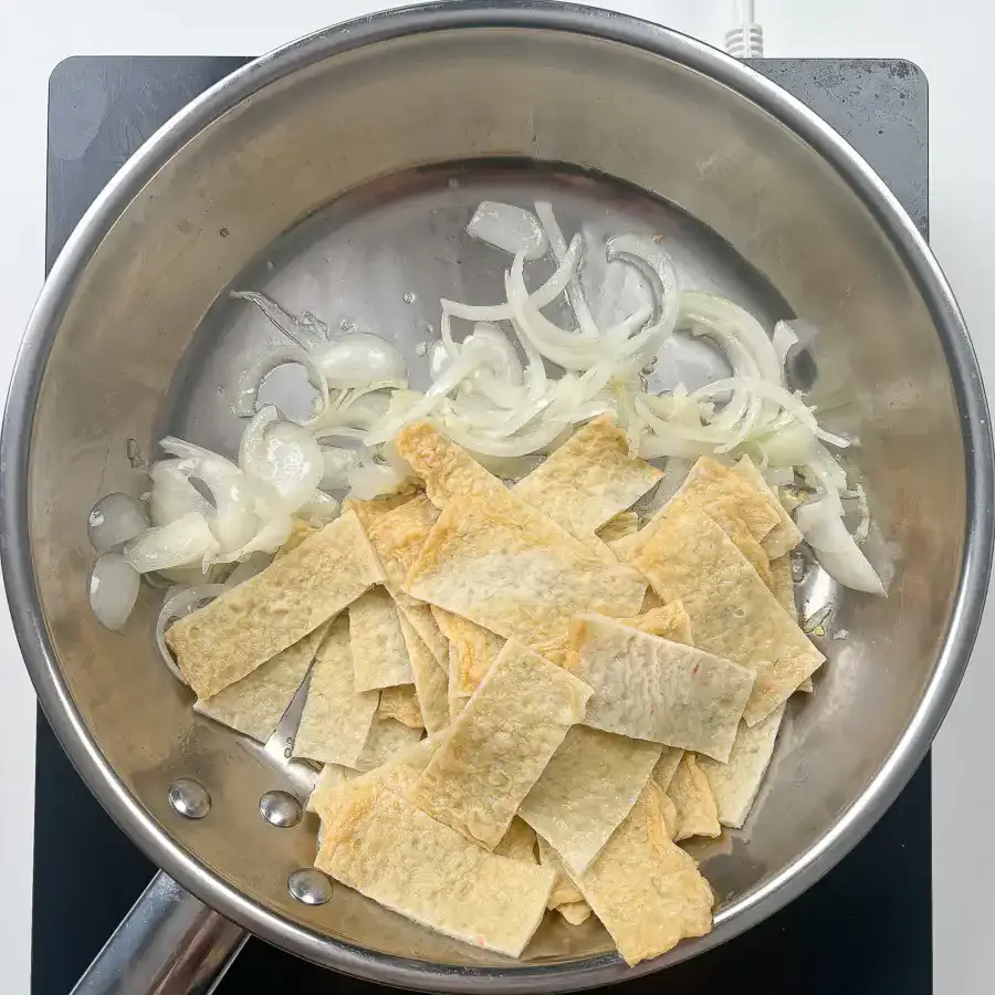 Stir fried fish cake being tossed with onion and garlic in a pan