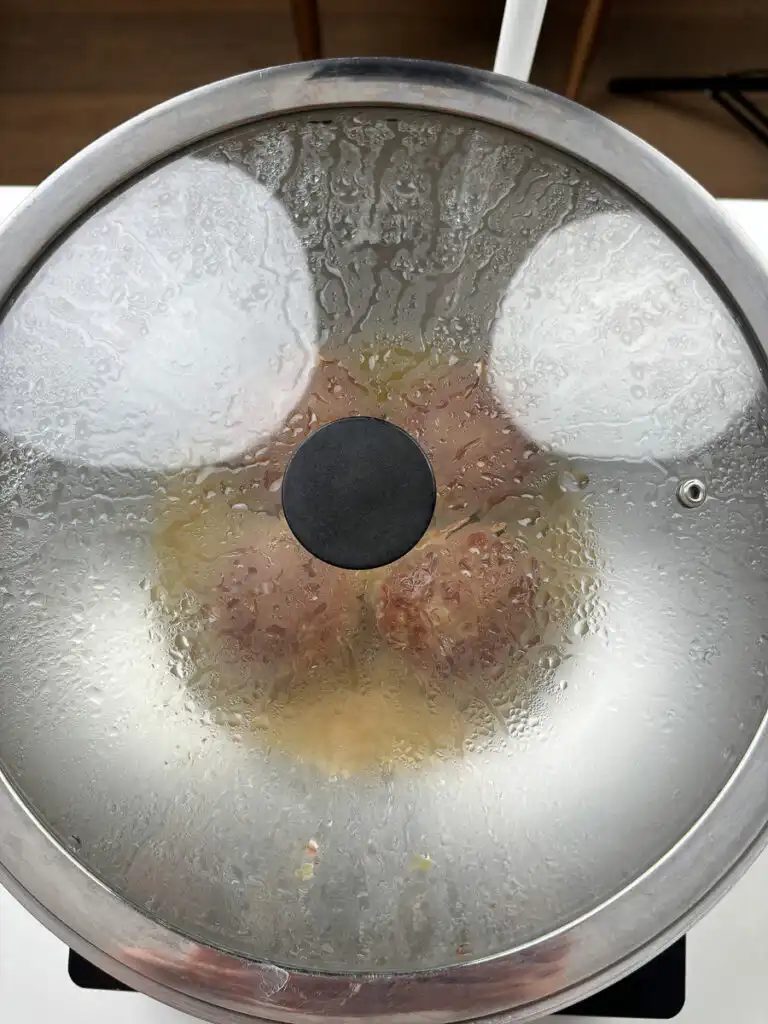 Tteokgalbi patties steaming under a covered lid with water added