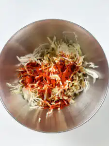 Tossing spicy cabbage salad with gochugaru sauce in a bowl
