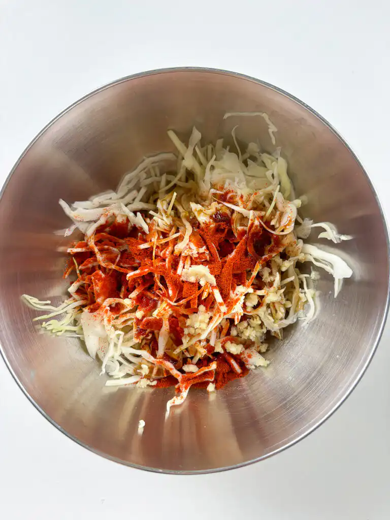 Tossing spicy cabbage salad with gochugaru sauce in a bowl
