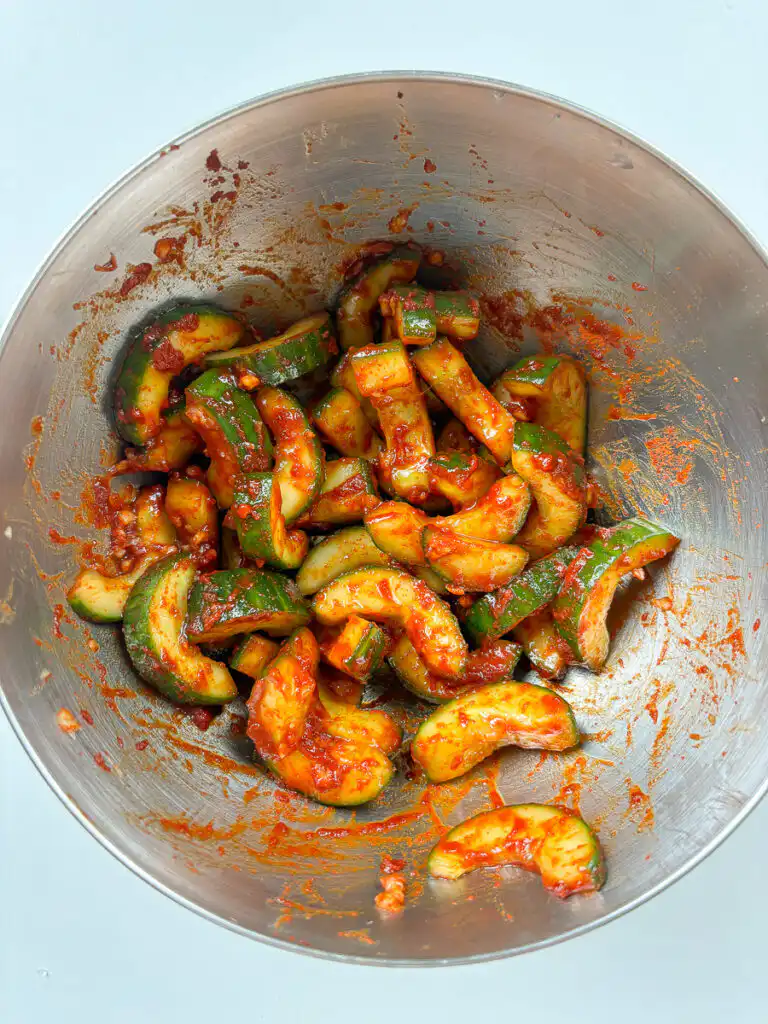 Cucumber cubes evenly coated in red gochugaru paste in a mixing bowl