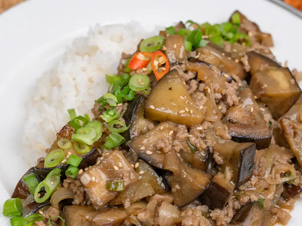 Close-up of glossy eggplant and ground meat sauce over steamed rice