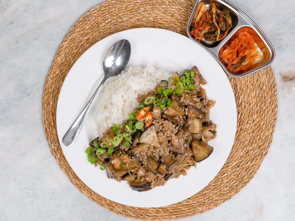 Spoonful of glossy eggplant and ground beef lifted from a rice bowl