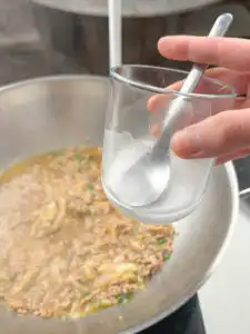 Potato starch slurry being added gradually to thicken the sauce