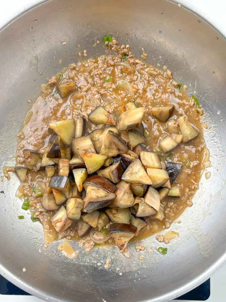 Seared eggplant added back into glossy oyster sauce in a pan