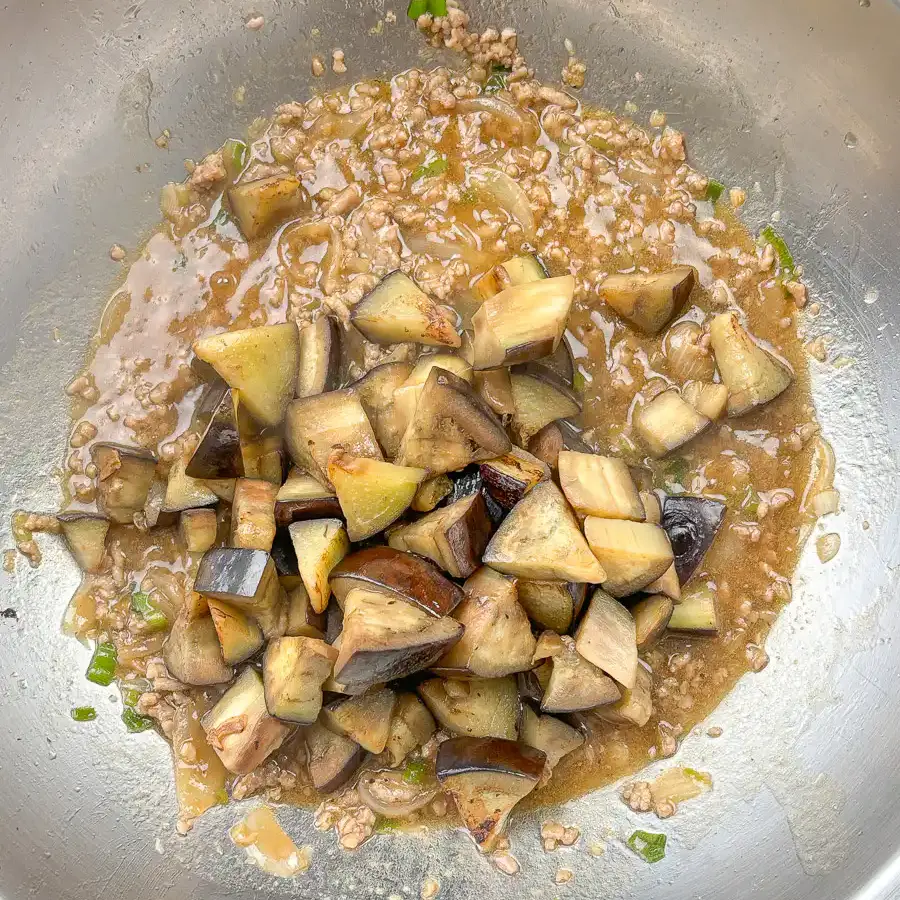 Seared eggplant added back into glossy oyster sauce in a pan