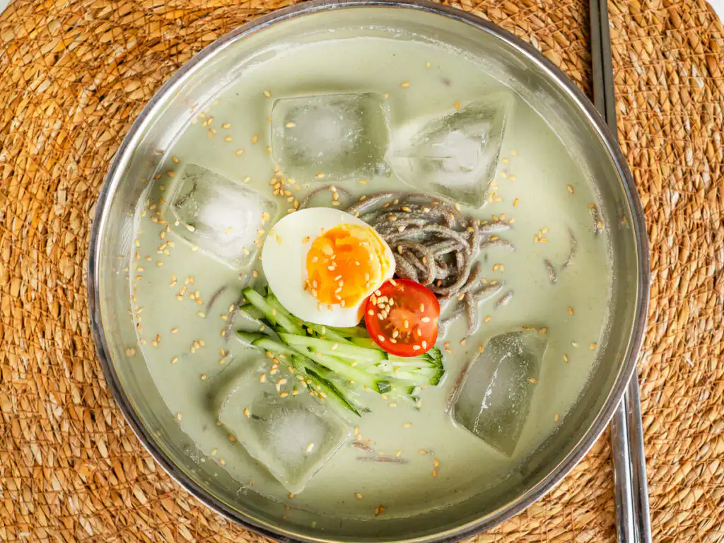 Korean cold noodles with matcha broth served in a stainless bowl with ice cubes