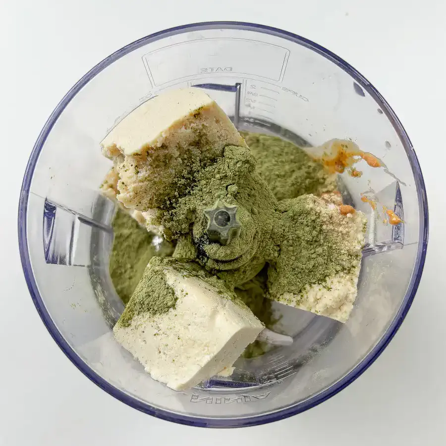 Tofu, matcha powder, and peanut butter being added to a blender for matcha kongguksu broth