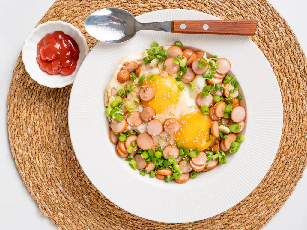 Sausage and Rice Recipe: 5-Min Korean Sausage Butter Rice Korean sausage butter rice in white ceramic bowl, a spoon and ketchup alongside.