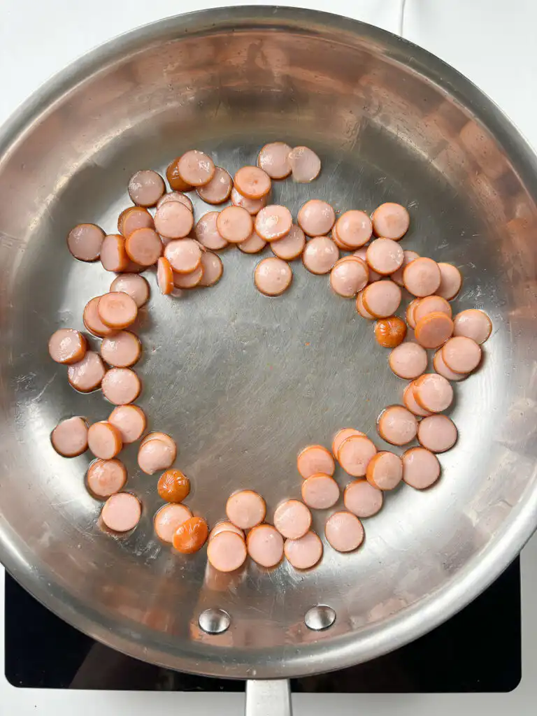 Sausage rounds sizzling in olive oil for easy sausage rice recipe, starting to turn golden