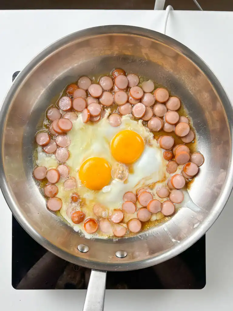 Egg frying in caramelised soy-butter sauce, lacy edges forming, yolk still runny, sausage butter rice process