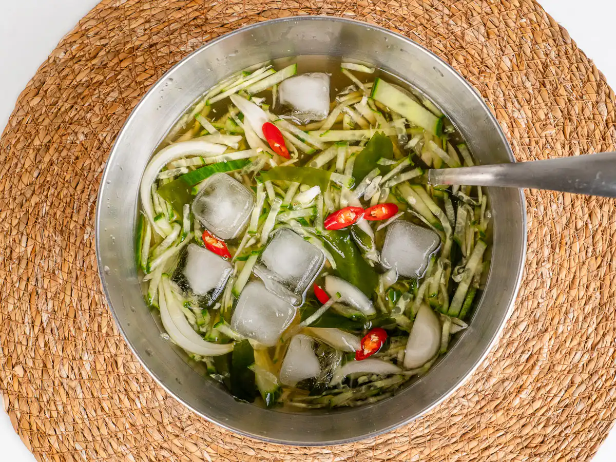 Oi naengguk topped with ice cubes and toasted sesame seeds and red pepper