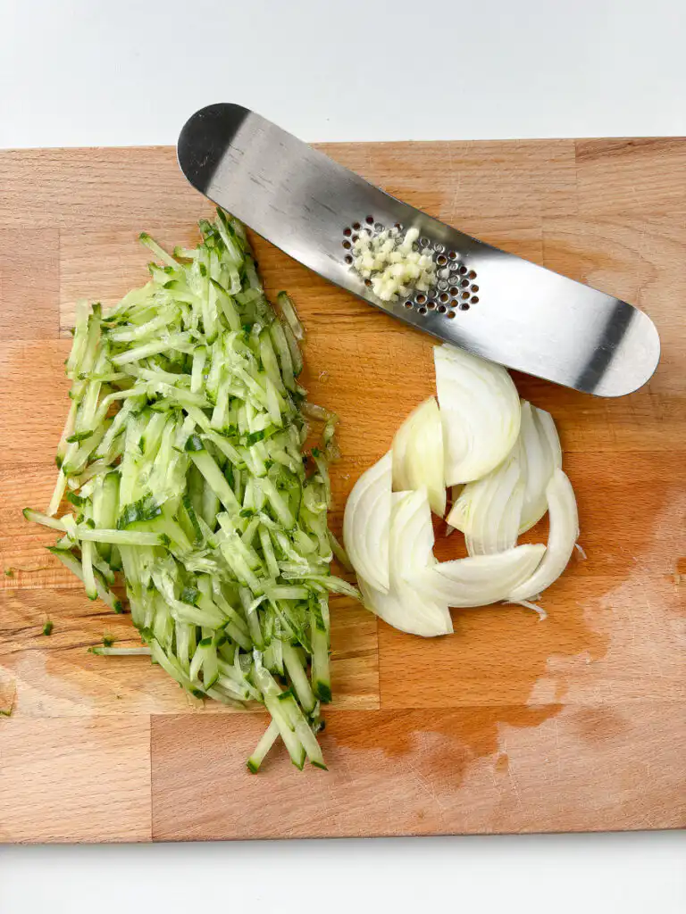 Julienned cucumber and thinly sliced onion on a cutting board for oi naengguk