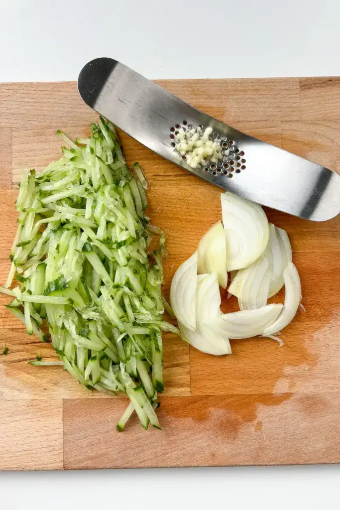 Korean Cucumber Soup (Oi Naengguk) - Best Cold Summer Soup Julienned cucumber and thinly sliced onion on a cutting board for oi naengguk