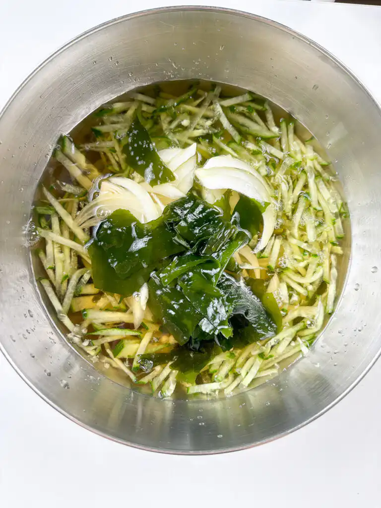 Adding julienned cucumber and onion to the oi naengguk broth