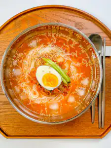 Traditional kimchi mari guksu in a stainless steel bowl with chopsticks
