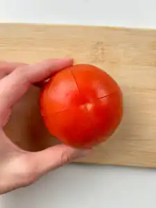 Tomato Gochujang Bibim Guksu - Summer Spicy Cold Noodles scoring a cross on the bottom of a fresh tomato before blanching