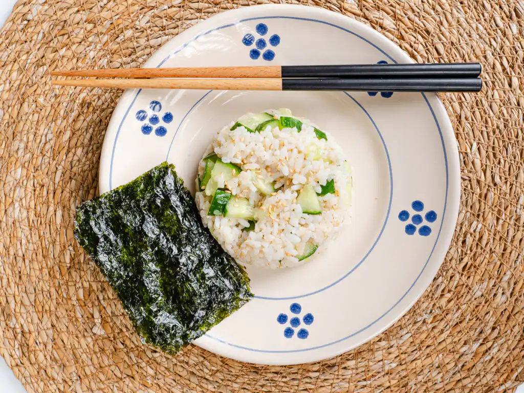 A side angle view of fresh cucumber cubes coated in toasted sesame oil and mixed with warm white rice.
