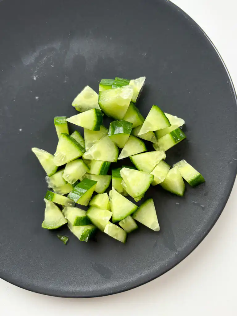 icing fresh English cucumber into small uniform cubes on a wooden cutting board.