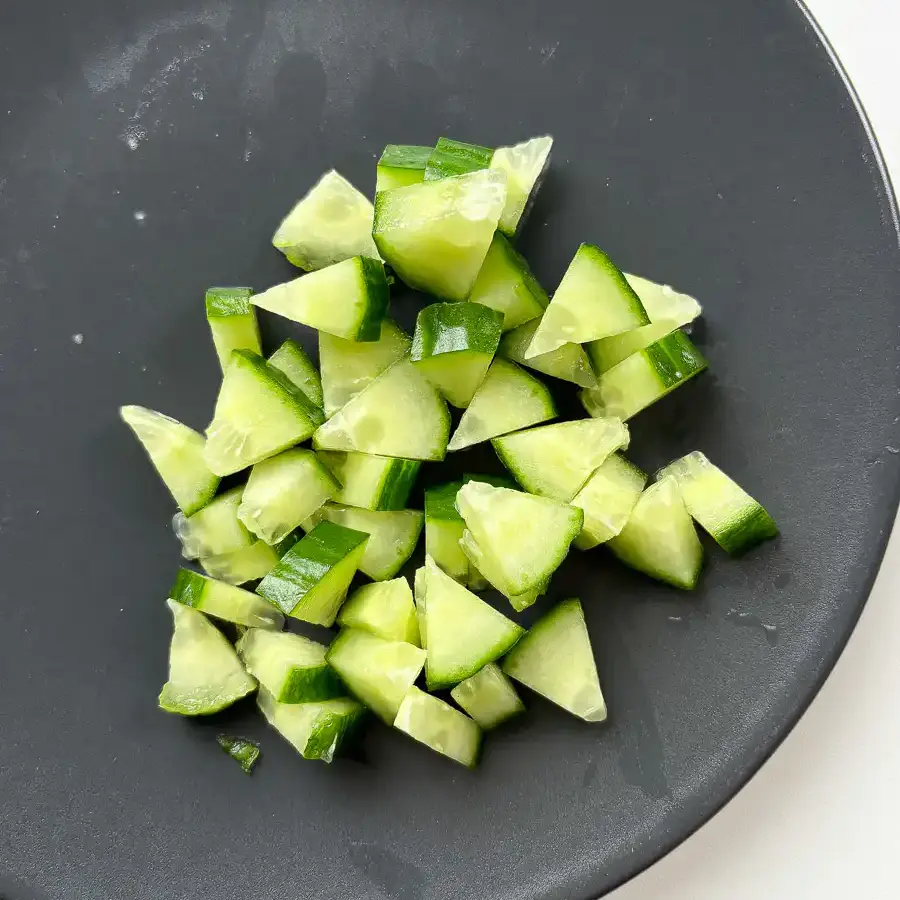 icing fresh English cucumber into small uniform cubes on a wooden cutting board.
