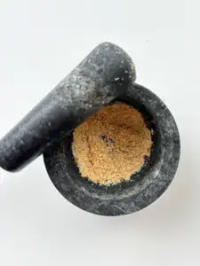 Grinding toasted sesame seeds in a small mortar to release rich nutty oils.