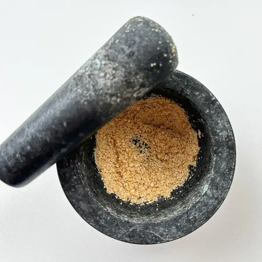 Grinding toasted sesame seeds in a small mortar to release rich nutty oils.