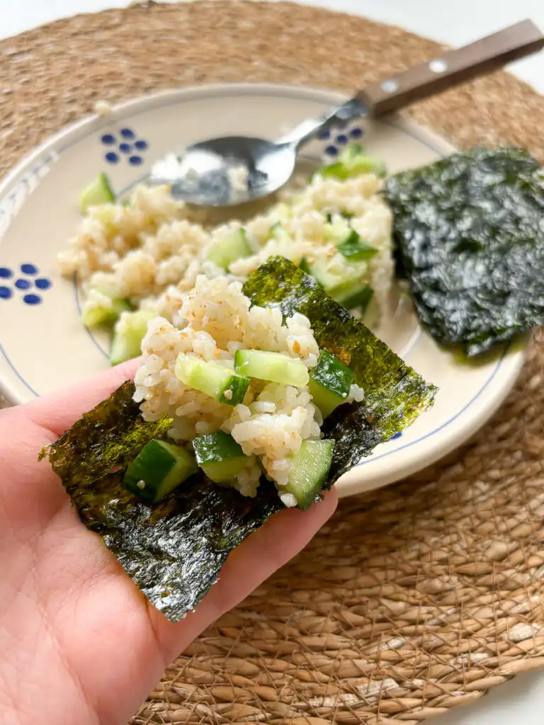 Hands wrapping seasoned cucumber rice in a crisp sheet of Korean roasted seaweed.