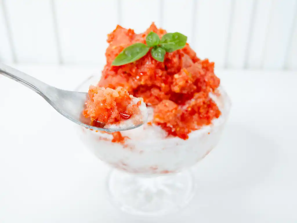 Tomato Bingsu: Easy Bingsu Recipe with Greek Yogurt Hand holding a spoon dipping into a freshly prepared tomato bingsu bowl.